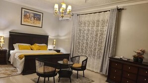 Une chambre à coucher comprenant un lit, deux chaises, une table de chevet, une commode et un lustre.