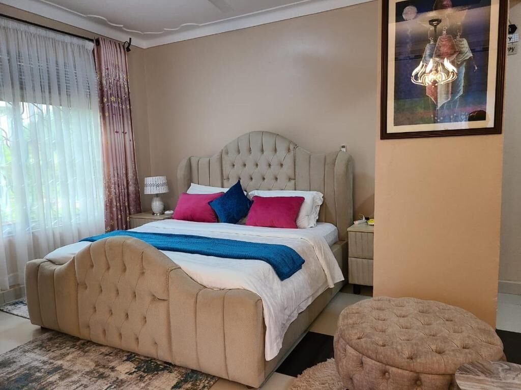 A bedroom with a large bed, a nightstand, a lamp, and a painting on the wall.