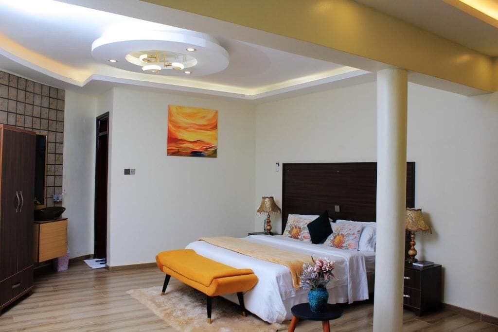 A modern bedroom with a bed, bedside tables, a nightstand, a bench, and a painting on the wall.