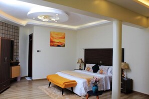 A modern bedroom with a bed, bedside tables, a nightstand, a bench, and a painting on the wall.