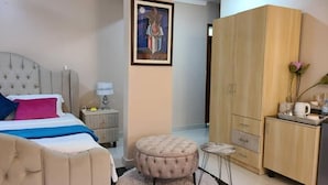 Une chambre à coucher comprenant un lit, une table de chevet, un pouf, une armoire et un tableau accroché au mur.