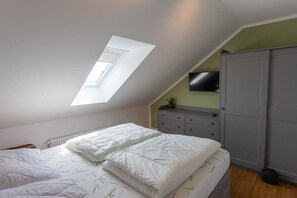 A bedroom with a sloped ceiling, a bed with white bedding, a dresser, and a television on the wall. - Small spruce tree with balcony (Braunlage)