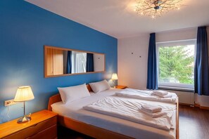 Ein Hotelzimmer mit einem großen Bett, einem Nachttisch mit Lampe, einem Spiegel und einem Fenster mit Vorhängen.