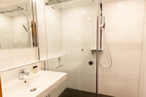Ein modernes Badezimmer mit einer gläsernen Duschkabine, einem weißen Waschbecken und einem großen Spiegel.