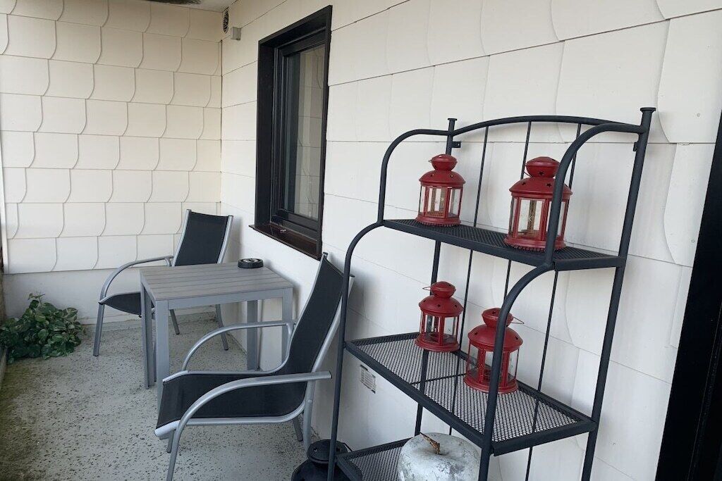 A patio area with a metal table and chairs, a metal shelf with red lanterns, and a window with a black frame.