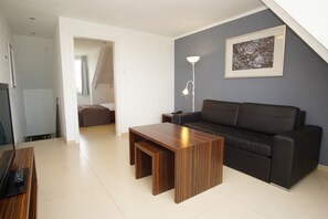 Een moderne woonkamer met een donkere bank, een houten salontafel en een vloerlamp.