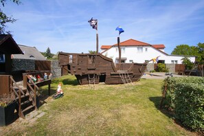 Een houten piratenschipmodel in een achtertuin met een huis op de achtergrond.