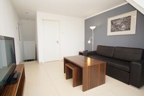 A modern living room with a dark-colored sofa, a wooden coffee table, a TV, and a floor lamp. - Near the beach, balcony, ocean view, Dranske beach vacation rentals, Vacation Rental 26 (Dranske)
