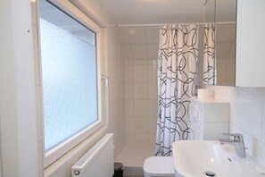 Une salle de bain avec une fenêtre, une douche, des toilettes et un lavabo.