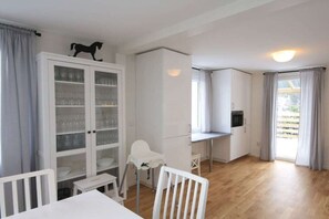 Une cuisine moderne avec des meubles blancs, un coin repas doté d’une table et de chaises blanches, et une vue sur l’extérieur par une fenêtre.