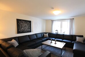 Un salon moderne avec un canapé d’angle en cuir noir, une table basse et des œuvres d’art abstraites accrochées au mur.