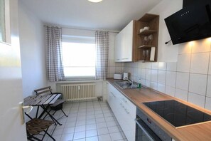 Une cuisine compacte dotée d’une cuisinière intégrée, d’une fenêtre avec des rideaux et d’un coin repas comprenant une table et des chaises.