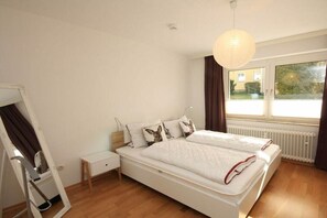 Une chambre à coucher comprenant un lit, une table de chevet, une lampe, une fenêtre et un radiateur.