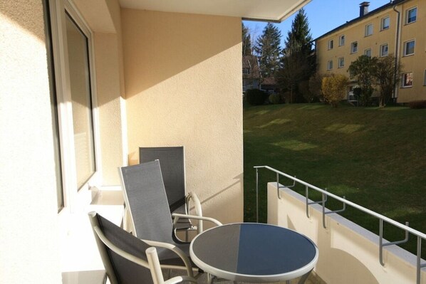 Un balcon avec une table et des chaises, donnant sur une pelouse bien entretenue et sur des bâtiments en arrière-plan.