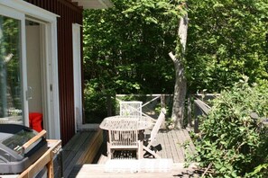 Une terrasse en bois avec une table et des chaises, un barbecue et une chaise rouge.