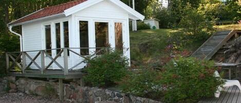 A small white building with a red roof, a wooden deck, and a stone wall.