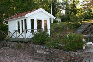 Un petit bâtiment blanc avec un toit rouge, une terrasse en bois et un mur en pierre.
