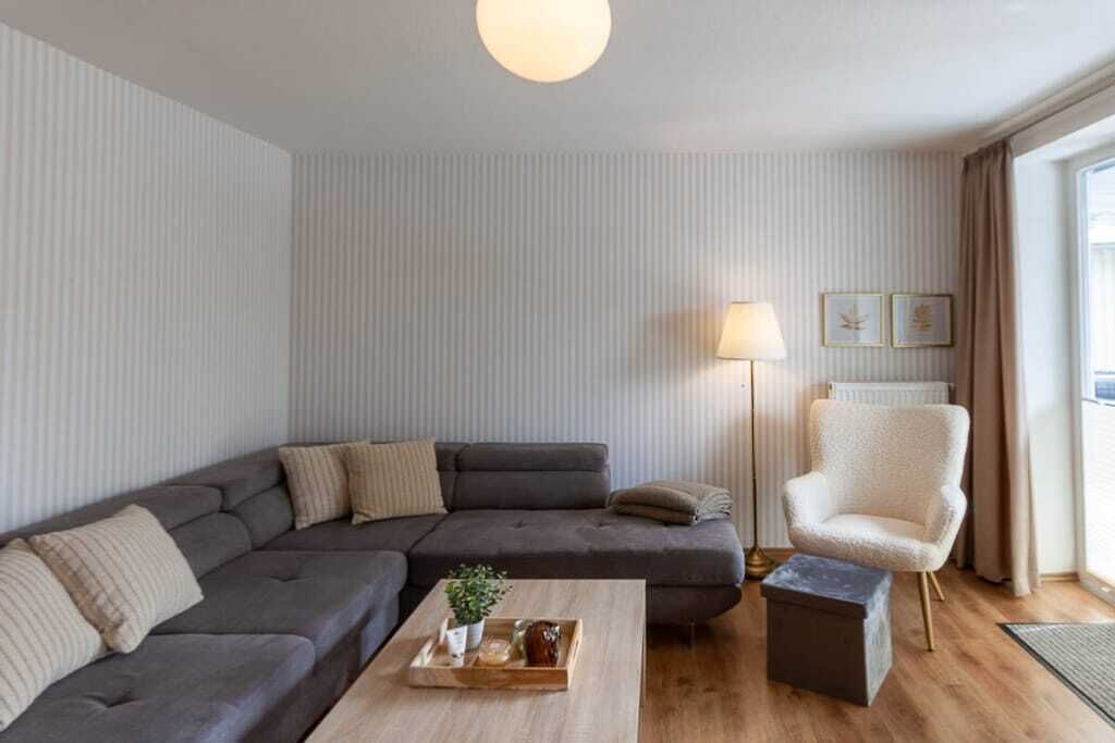 En moderne stue med en hjørnesofa, et lille bord med bakke, en gulvlampe og en stol.