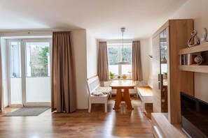Ein modernes Wohnzimmer mit Holzboden, einem Esstisch, zwei weißen Sofas, einem Fernseher und einem Bücherregal.