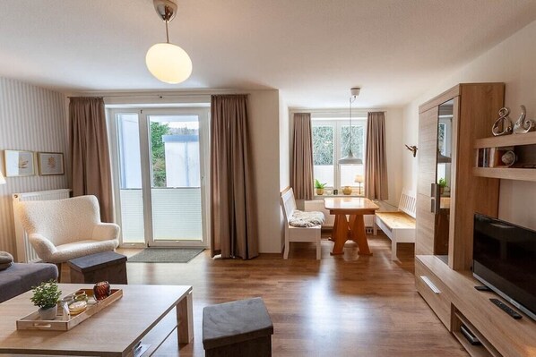 Ein modernes Wohnzimmer mit Sofa, Couchtisch, Fernseher und einem Essbereich mit Tisch und Stühlen.