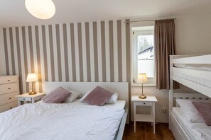 Ein Schlafzimmer mit einem Einzelbett, zwei Nachttischen mit Lampen, einem Fenster mit Vorhängen und einem Etagenbett rechts.