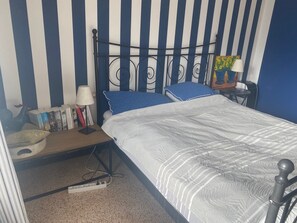 Ein Schlafzimmer mit Bett, Nachttisch, Lampe, Bücherregal und einem Bild an der Wand.