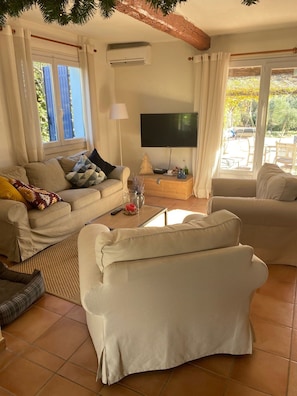Ein Wohnzimmer mit einer Couch, einem Couchtisch, einem Fernseher und einem Fenster mit Vorhängen.