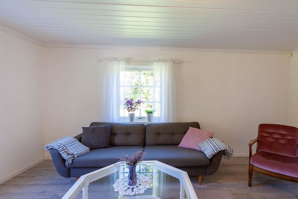 A living room with a grey sofa, a red chair, and a glass coffee table with a vase.