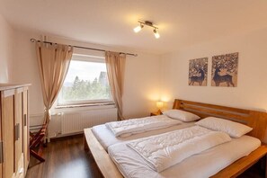 Een slaapkamer met twee bedden, een raam met gordijnen, een radiator en een muur met twee dieren schilderijen.