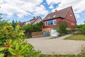 Een rode woning met een schuin dak, een verharde oprit en een houten hek.