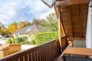 Un balcon en bois avec une table et une chaise, donnant sur un quartier résidentiel avec des maisons et des arbres.