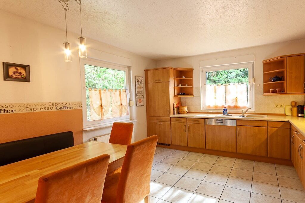 A kitchen with wooden cabinets, a dining table with chairs, and a window with curtains.