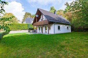 Une maison moderne à deux étages, dotée d’un toit en pente, d’un patio couvert et d’une pelouse bien entretenue.