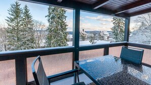 Quarto com mesa e cadeiras de vidro, vista para árvores cobertas de neve e teto de madeira.