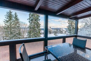 Une pièce avec une table et des chaises en verre, une vue sur des arbres couverts de neige et un plafond en bois.