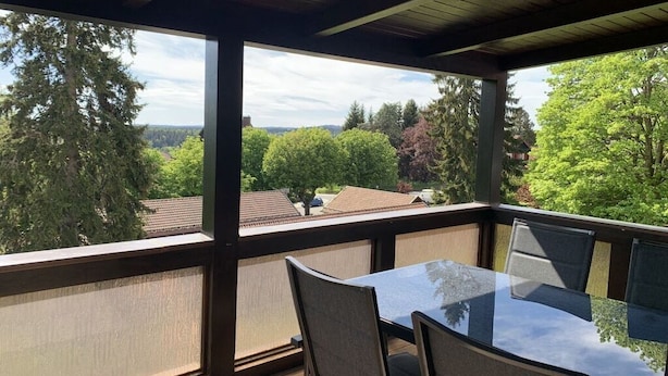Varanda com mesa e cadeiras, vista para área residencial com árvores e casas.