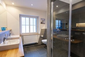 Une salle de bain moderne dotée d’une douche à parois de verre, d’un meuble-lavabo à deux vasques et d’une grande fenêtre laissant entrer la lumière naturelle.