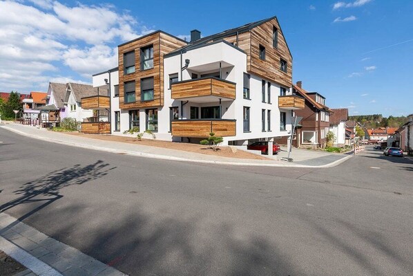Un immeuble résidentiel moderne à plusieurs étages, doté de balcons, d’un toit plat et donnant sur la rue.