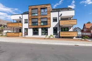 Un immeuble résidentiel moderne à plusieurs étages, doté d’un toit plat, de grandes fenêtres et de panneaux en bois décoratifs.