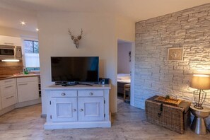 A modern living room with a flat-screen TV on a white cabinet, a stone wall, and a wicker basket with a lamp. - Small mountain suite (Braunlage)