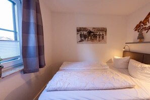 A bedroom with a bed, a window with curtains, a wall-mounted picture, and a shelf with a lamp. - Small mountain suite (Braunlage)