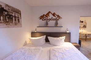 Ein Hotelzimmer mit Bett, einem Kopfteil, einem an der Wand befestigten Regal mit Bergdeko und einem gerahmten Bild.