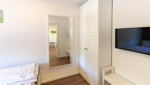 Quarto com cama, guarda-roupa, televisão na parede e espelho refletindo o ambiente.