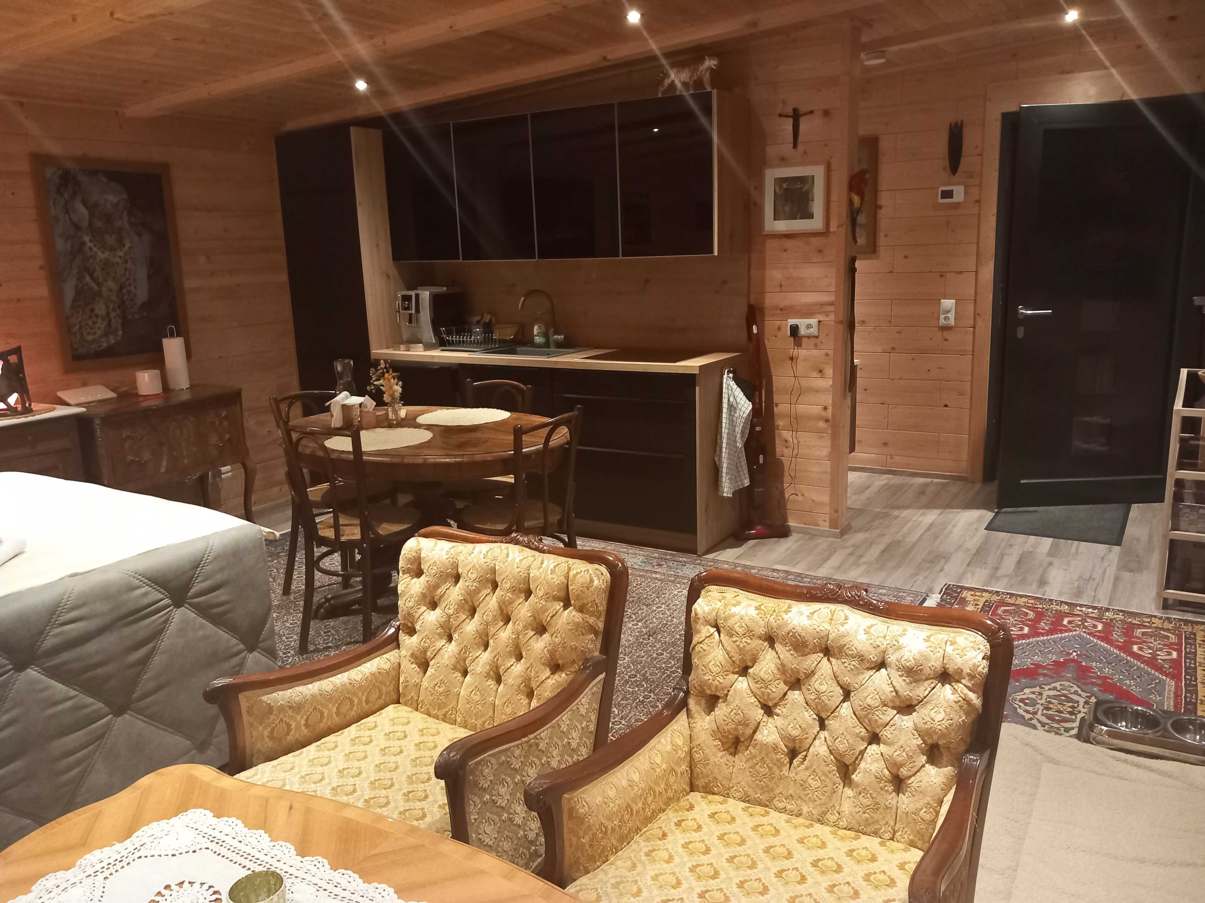 A cozy room with a bed, a dining table with chairs, a kitchen area, and a small altar.