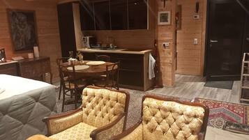 A cozy room with a bed, a dining table with chairs, a kitchen area, and a small altar.