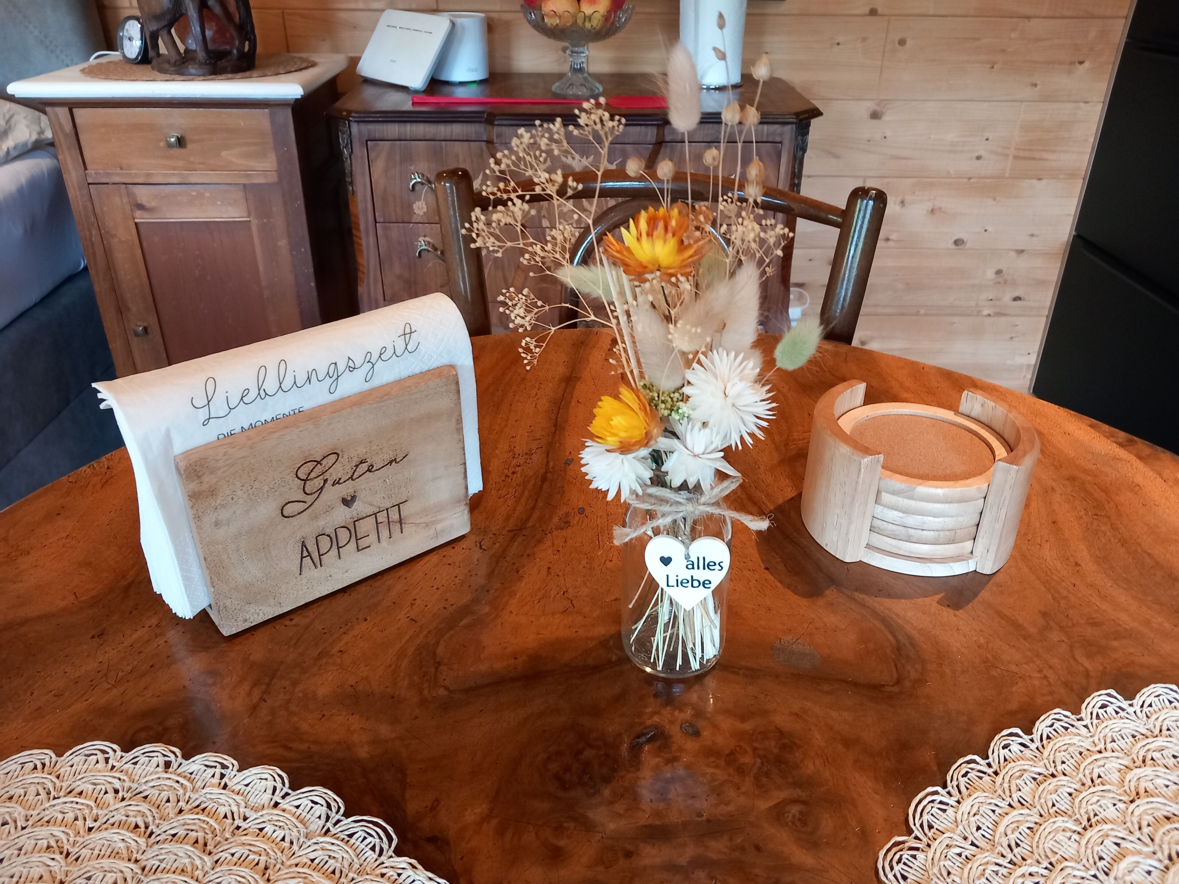 Una mesa de madera con un jarrón de flores, un letrero de madera y un mantel tejido.