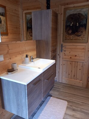 Interior de una cabaña de madera con un lavabo blanco, armarios de madera y un cuadro de un elefante.