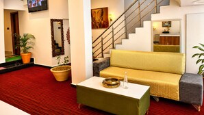 Un vestíbulo de hotel con alfombra roja, un sofá, una mesa de centro, una escalera y un televisor montado en la pared.
