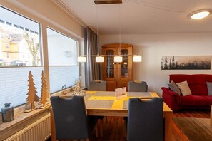 Ein Essbereich mit einem Holztisch, vier Stühlen, einem roten Sofa und einem Schrank mit Glastüren.