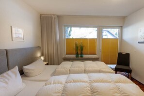 Ein Hotelzimmer mit Bett, einem Sessel, einem Fenster mit Jalousien und einem Bild an der Wand.